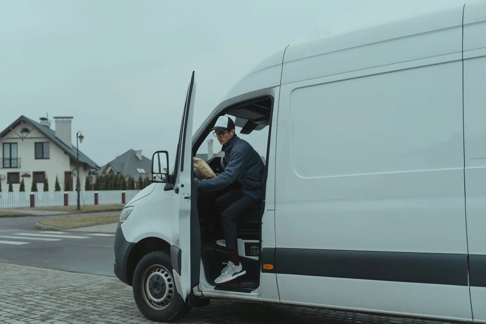 A courier stepping out of a white delivery van on a residential street