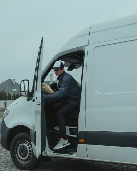 A courier stepping out of a white delivery van on a residential street