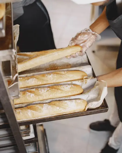 A baker in gloves arranging fresh baguettes on a rack