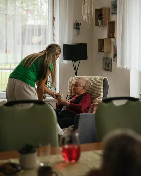 A caregiver serving tea to residents in a bright nursing-home lounge