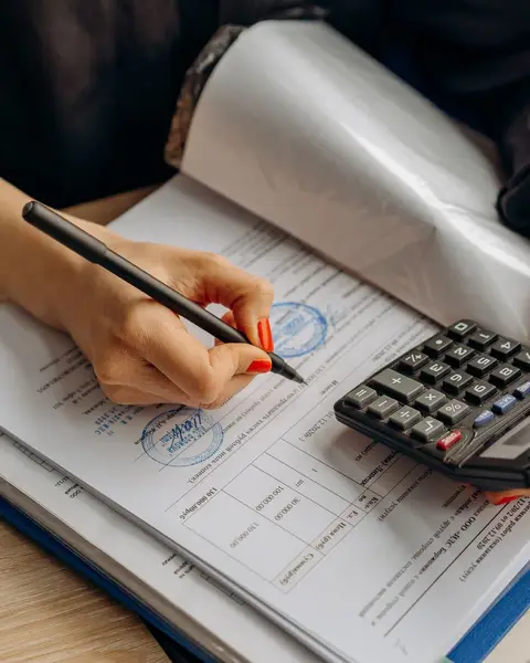 Hands working through invoices with a calculator at an office desk