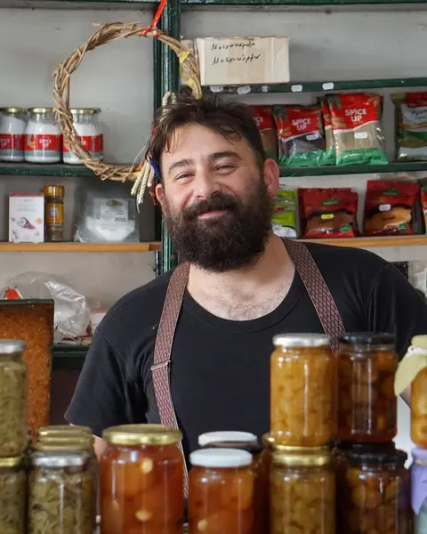 A smiling shopkeeper behind shelves of homemade preserves